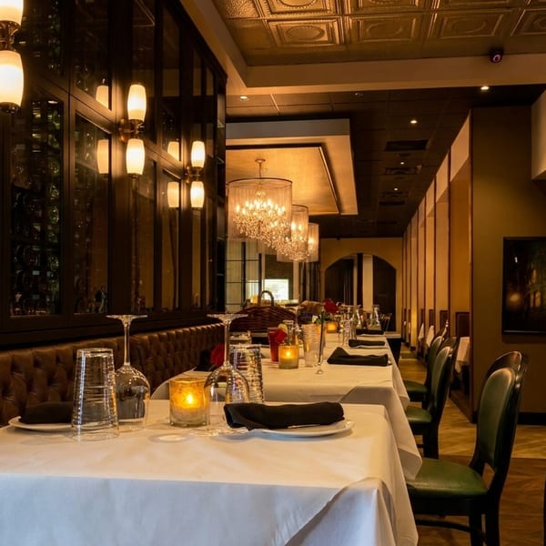 Elegant restaurant interior with white-clothed tables, leather banquettes, wine displays, and chandeliers.