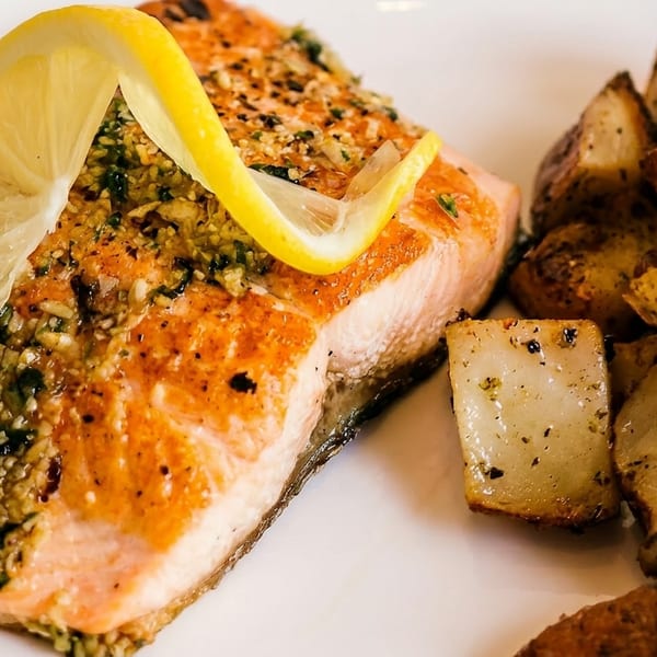 Close-up of a salmon fillet with herbs and lemon, served with roasted potatoes.