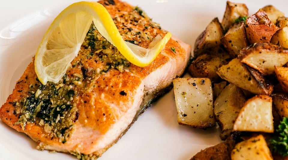 Close-up of a salmon fillet with herbs and lemon, served with roasted potatoes.
