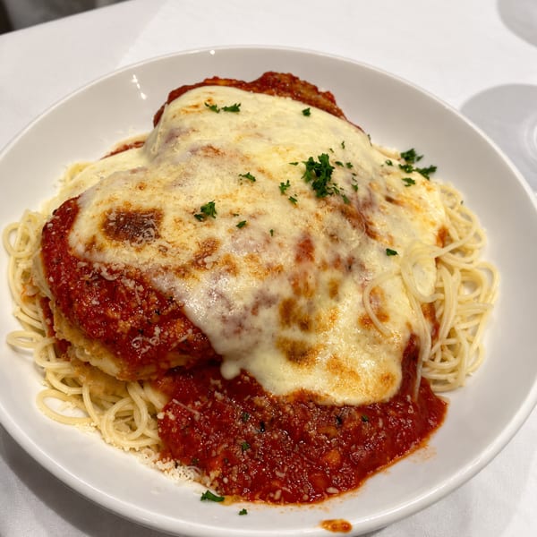 Chicken parmesan with melted cheese and marinara sauce, served over spaghetti on a white plate.