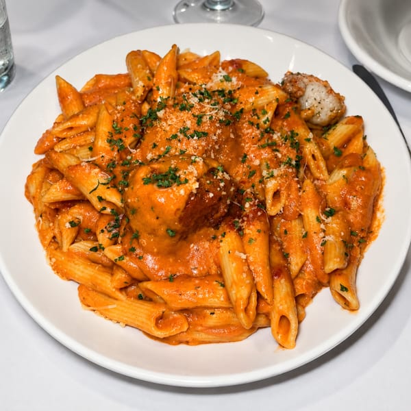 Penne pasta with meatballs in a creamy tomato sauce, topped with parsley and parmesan cheese.