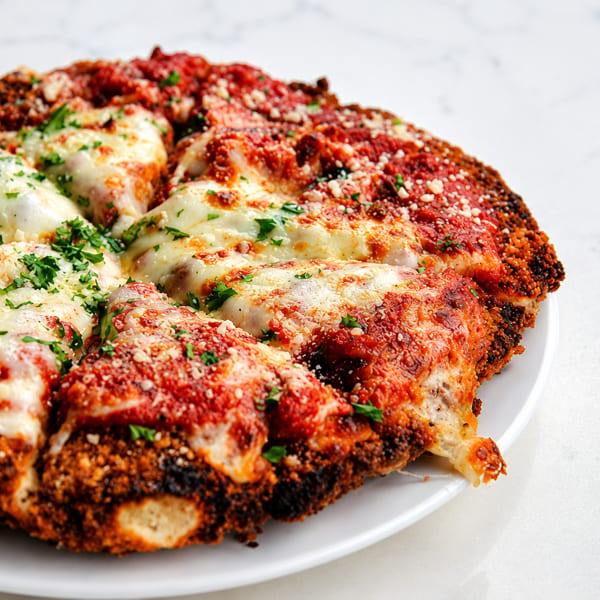 Close-up of a deep-dish pizza with melted mozzarella, red sauce, and parsley on a white plate.