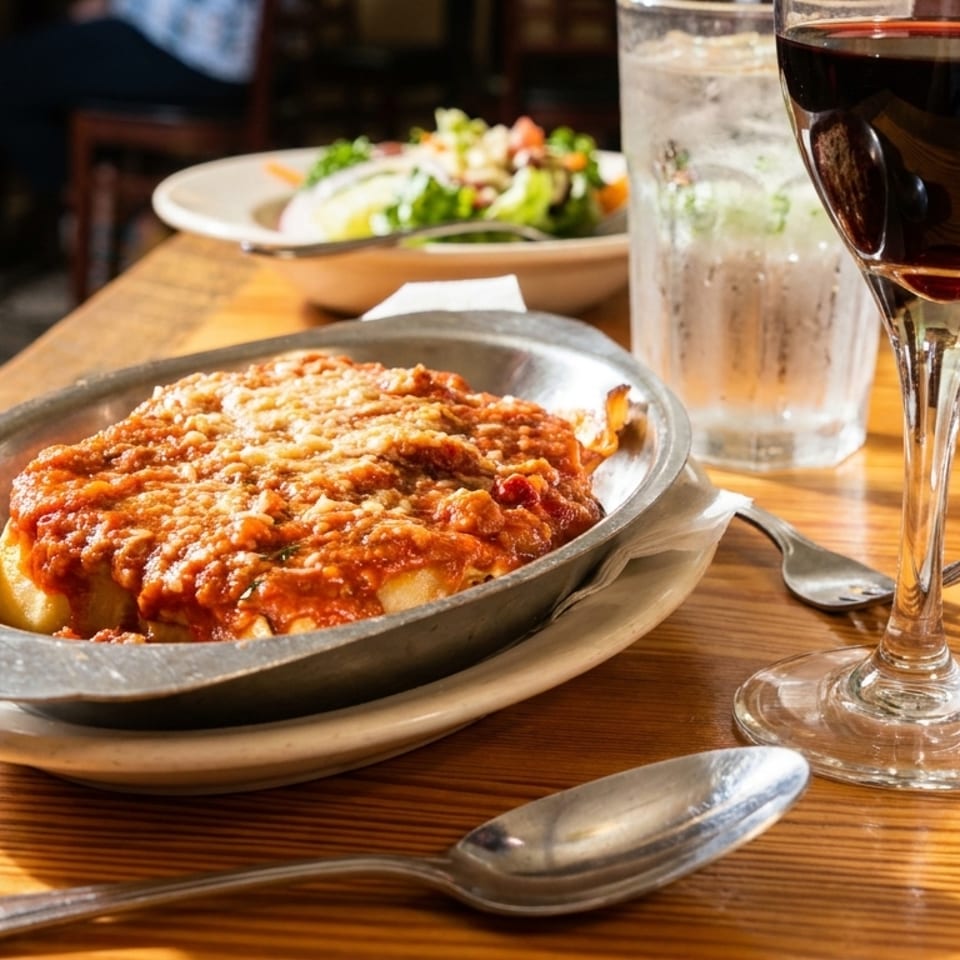 Baked pasta with red sauce and melted cheese, a glass of red wine, and a salad on a wooden table.
